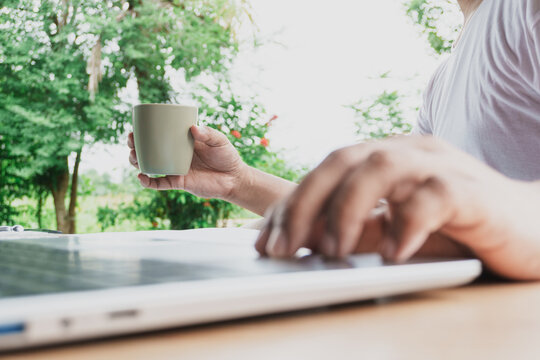 Relaxed remote worker taking a coffee break while using laptop outdoors in a natural green environment, promoting work life balance, productivity, flexible working, mindful focus and healthy lifestyle