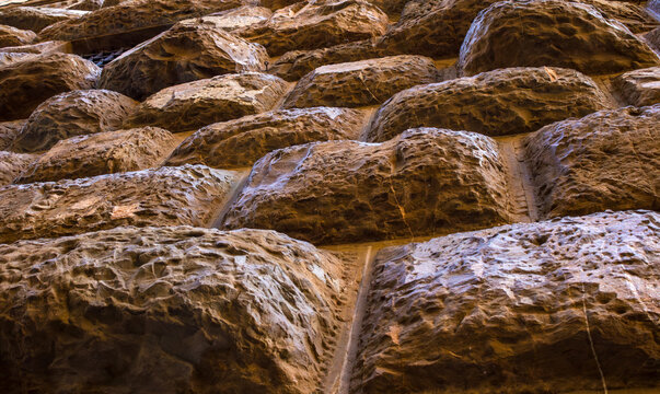 Rough-hewn stone blocks of a rusticated masonry wall in raking light. Craftsmanship and durability of historical stonework.