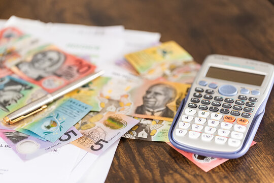 Pen and Australian banknotes with invoices and calculator on desk