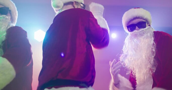 Santa claus group dance at christmas party. Dancers in costumes with beards and sunglasses groove under disco lights creating funny festive vibes for ads and events. Bold Xmas party fun theme.