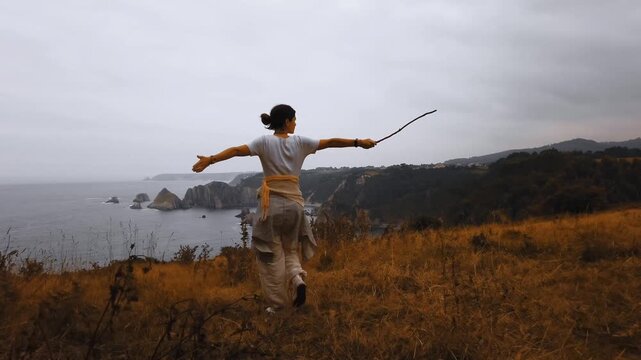 Model woman standing at a coastal viewpoint above rocky Asturias cliffs and sea