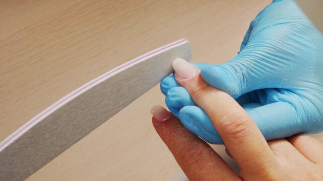 Manicurist files the shape of the nails with a special nail file, close up view. The manicurist shapes the nails with a nail file. The process of nail care in a beauty salon. Nail file processing.