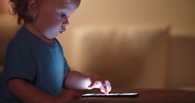 Child presses on the mobile phone screen, soft focus. Small baby presses by finger on the touch screen of the phone, close-up.  Little child learns to use modern technologies. Baby and cellphone.