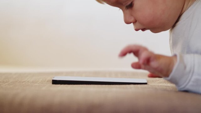 Small Baby pressing and  scrolling with finger on phone touch screen.  Little child  tapping on mobile phone screen. Little child learns to use new  internet technologies, close-up and soft focus