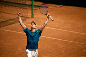 Fototapeta premium Tennis player celebrating victory on clay court with arms raised. Concept of tennis victory moment, sports motivation campaigns, winning emotion and summer tournament success.