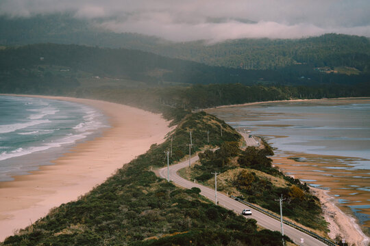 Winding coastal road curves between a sandy beach and a calm tidal inlet