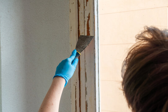 Woman Removing Old Paint from Wooden Window Frame with Putty Knife