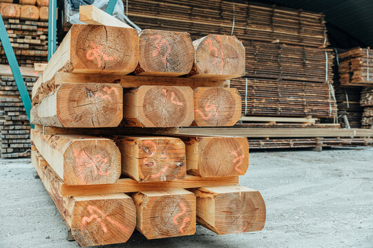 Close-up of stacked rough-sawn timber beams with marked end grain stored on spacers inside a sawmill warehouse. Visible wood texture and organized lumber inventory