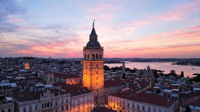Aerial view of a historic stone tower illuminated at sunset in an old european city with redtiled roofs and a waterfront