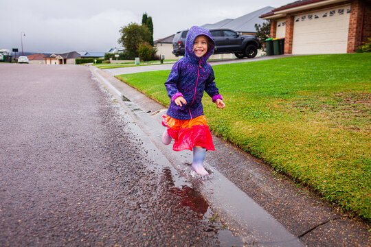 Happy child running and splashing through roadside gutter full of water on rainy autumn day