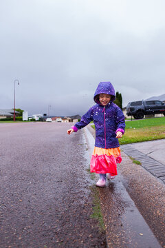 Happy child running and splashing through roadside gutter full of water on rainy autumn day
