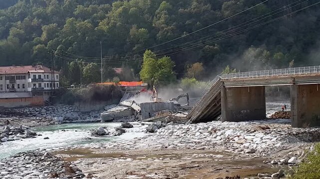 Demolition of collapsed bridge over mountain river with heavy machinery.