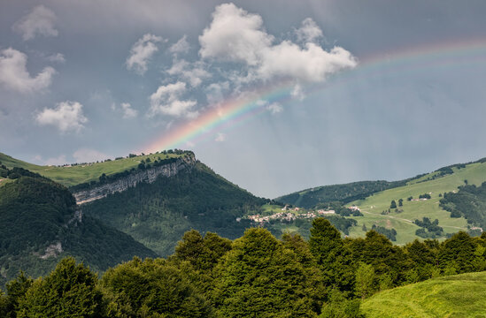 Rainbow arches over the lush green mountain landscape, highlighting a serene outdoor tourism destination for nature exploration in Brentonico, Monte Baldo Natural Park, Trentino, Italy.