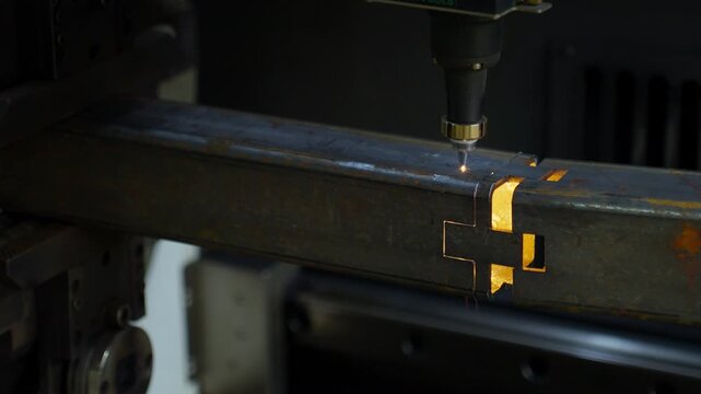 Laser cutting of rusted steel beam creating rectangular slots with molten glow, bright sparks and precise industrial machining inside dim workshop during fabrication
