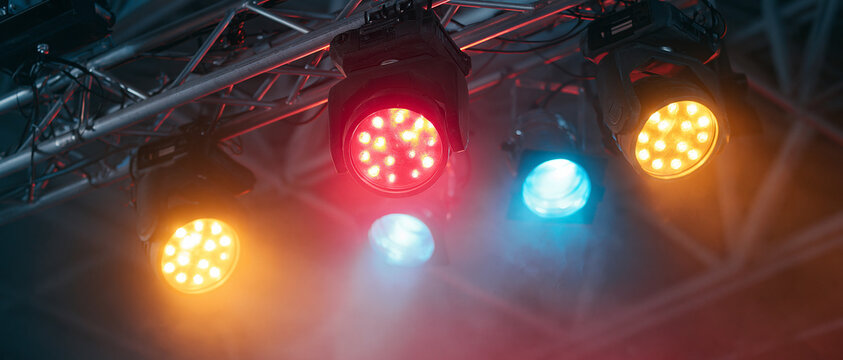 Stage lights illuminating a dark concert venue with colorful beams of light and haze.