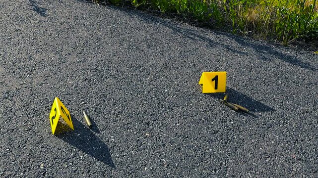Yellow evidence markers indicating the location of bullet casings on the asphalt at a crime scene, symbolizing a police investigation into a violent shooting or murder