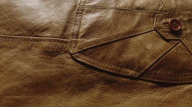 Slow reveal of a brown leather jacket featuring stitched seams and button pockets, emphasizing quality construction and timeless fashion design.