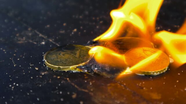 European currency, euro cent coins, engulfed in flames on a dark surface representing the concept of financial crisis, inflation, economic instability, and the devaluation of money