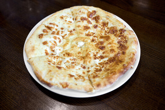 Traditional Megrelian khachapuri on plate; circular cheese-filled flatbread featuring golden baked crust, bubbling melted sulguni topping, and savory aroma from regional Georgian cuisine.