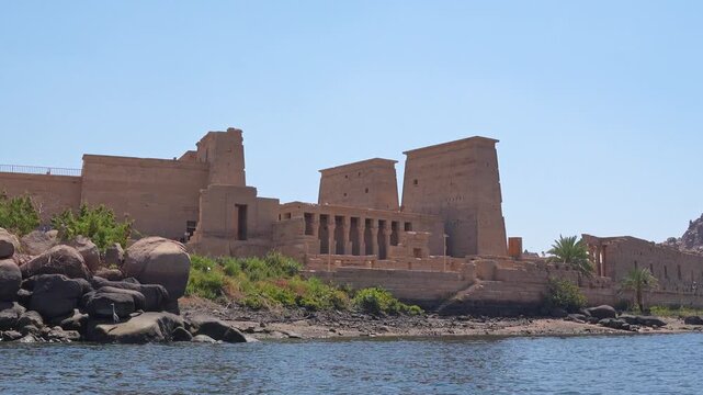 Boat slowly navigating along the philae temple complex on agilkia island. Historic egyptian architectural landmark on the nile river near aswan