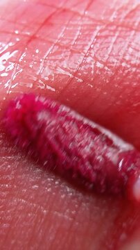 Vertical extreme close up of pink lip tint brush applicator on lip skin surface. Suitable for beauty product theme, makeup application concept.