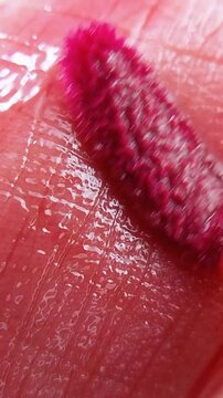 Extreme close up of lip skin surface being applied with pink lip tint liquid using a brush. Makeup application, beauty product concept with soft pigment texture.