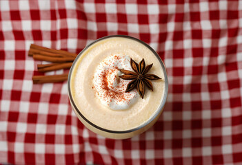 Fototapeta premium Top view of eggnog with whipped cream and star anise on plaid tablecloth