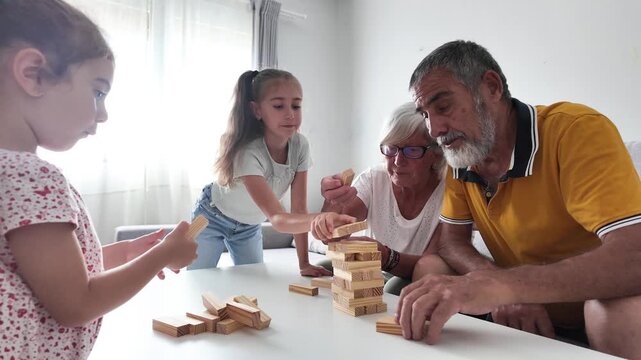 Happy Grandparents Playing Wooden Block Tower Game with Their Granddaughters