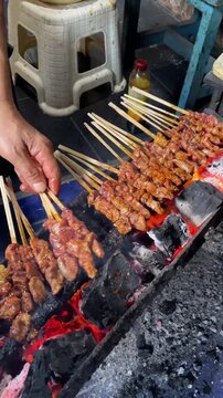 Indonesian street food vendor grilling traditional mutton satay (sate kambing) over hot charcoal embers, vertical shot