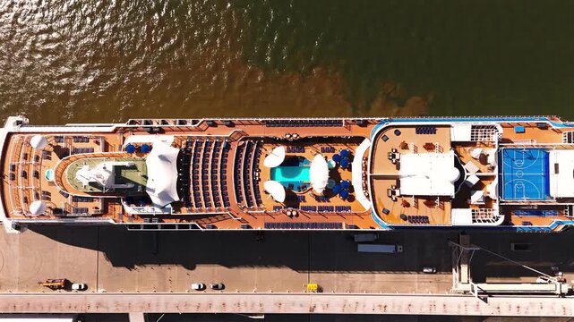 A large cruise ship rests at a waterfront terminal with pools sun decks and a helipad under calm harbor skies