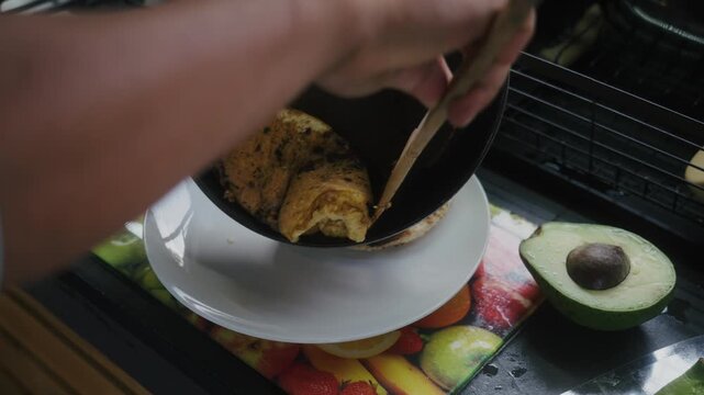 A person serving a nutritious and complete Colombian or South American breakfast featuring an omelet, arepa, and avocado