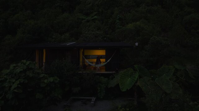 Aerial drone view of a tiny house-style cabin nestled in the mountains amidst lush nature, with a person walking nearby