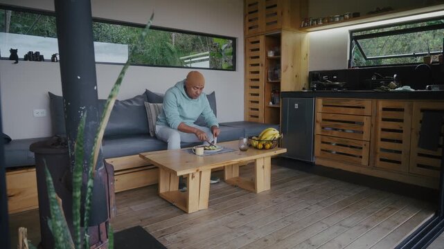 Latino man at home, eating and thinking while gazing into the distance in tiny house in nature landscape