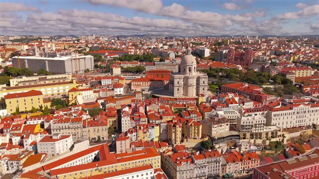 A drone orbits left around a domed landmark revealing layered rooftops and a bright blue sky