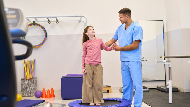 Child physiotherapy session, therapist assisting girl on trampoline for balance training, pediatric rehabilitation exercises in clinic, physical therapy session, motor skills development