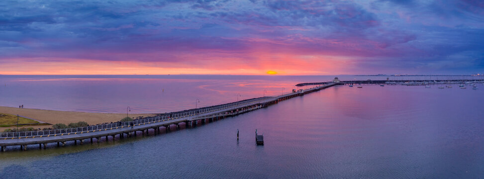 Aerial panorama view of a colourful sunset over a long marina jetty running towards the horizon