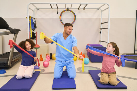Children's Rehabilitation: Therapist Assisting Kids with Resistance Band Exercises in Pediatric Physiotherapy Session, Motor Skills Training, and Balance Training in Rehab Center