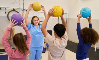Pediatric physiotherapy session with therapist and children doing exercises with colorful balls, rehabilitation and motor skills training in pediatric rehab center © Robert Kneschke
