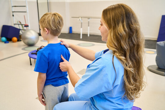 Pediatric Physiotherapist Assessing Child's Back Posture in Rehabilitation Center, Physical Therapy Session for Kids, Motor Skills Training, Exercise and Rehabilitation Equipment, Indoors