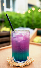 Obraz premium Colorful layered iced drink served in a glass with a straw on a wooden table at an outdoor cafe. Refreshing summer beverage. Copy space. Selective focus.