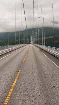 Car driving on a long bridge in Norway with misty mountains ahead.