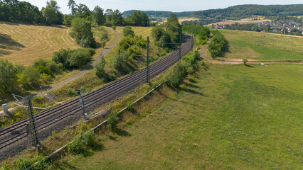 Fototapeta premium Aerial view of railway line winding through rural countryside with fields, forest and distant village