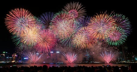 Fototapeta premium At midnight, colorful fireworks light up the night sky above a bustling city skyline during New Year’s celebrations.