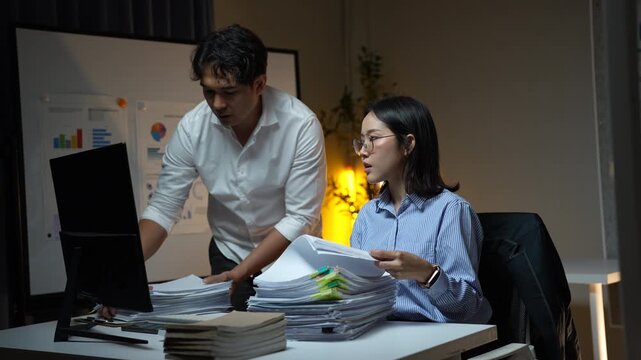 Stressed colleagues working late at night in a dark office, collaborating on a project with a huge pile of documents, feeling exhausted and overwhelmed by the heavy workload