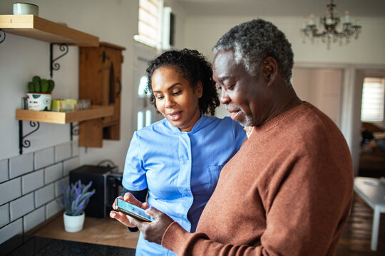 Home caregiver helping senior man with smartphone in kitchen