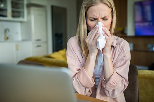 Sick woman sneezing into tissue at home office