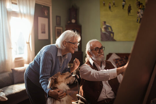 Senior couple painting together at home with dog