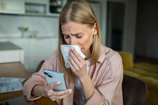 Sick woman using smartphone at home kitchen table