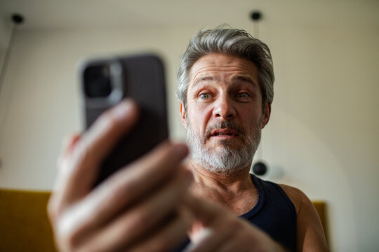 Middle-aged man reacting to shocking message on smartphone at home