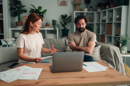 Couple discussing financial problems, managing household budget, and reviewing bills with laptop in living room